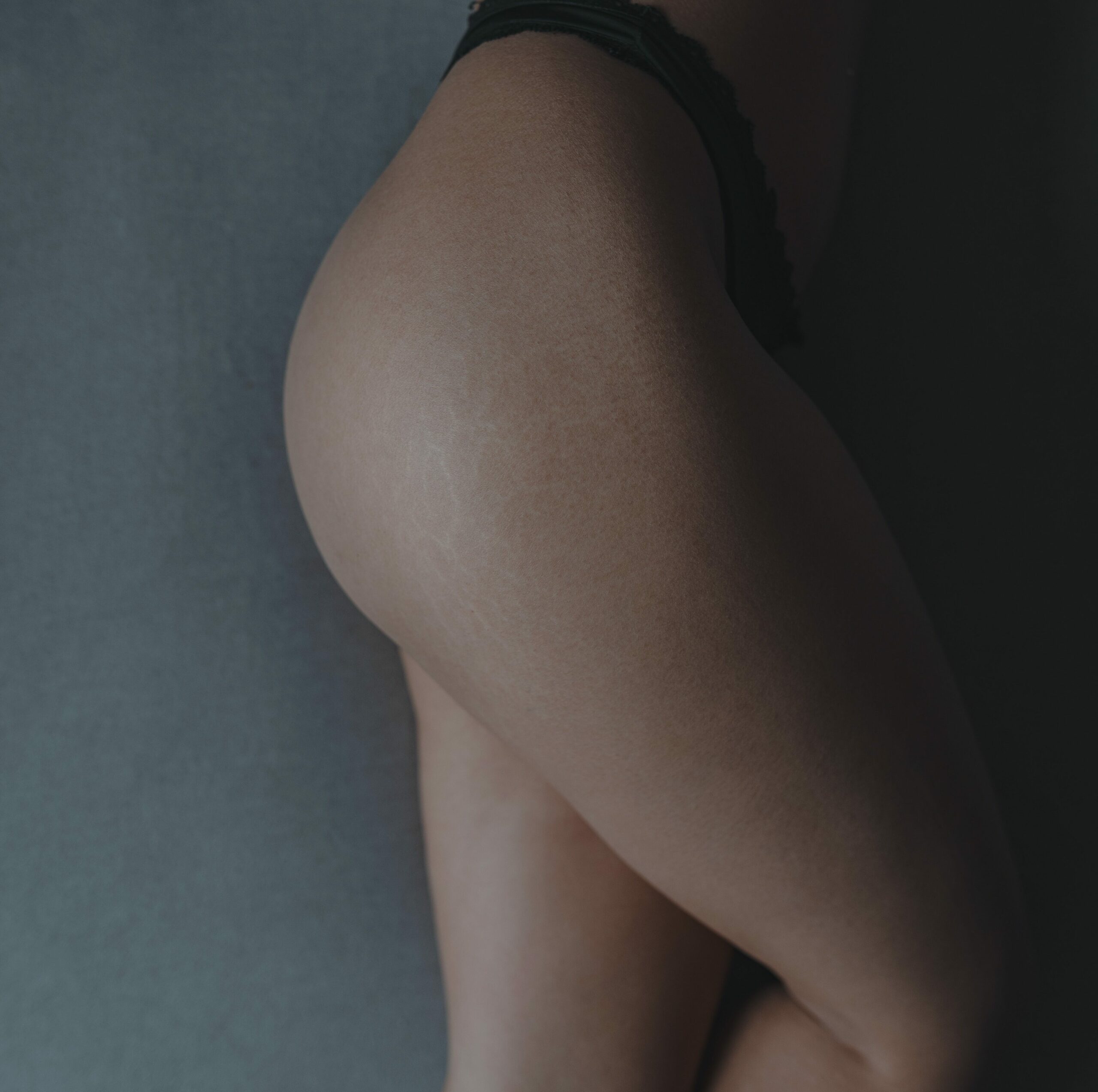 Kvinne i bare undertøy ligger på en grå bakgrunn